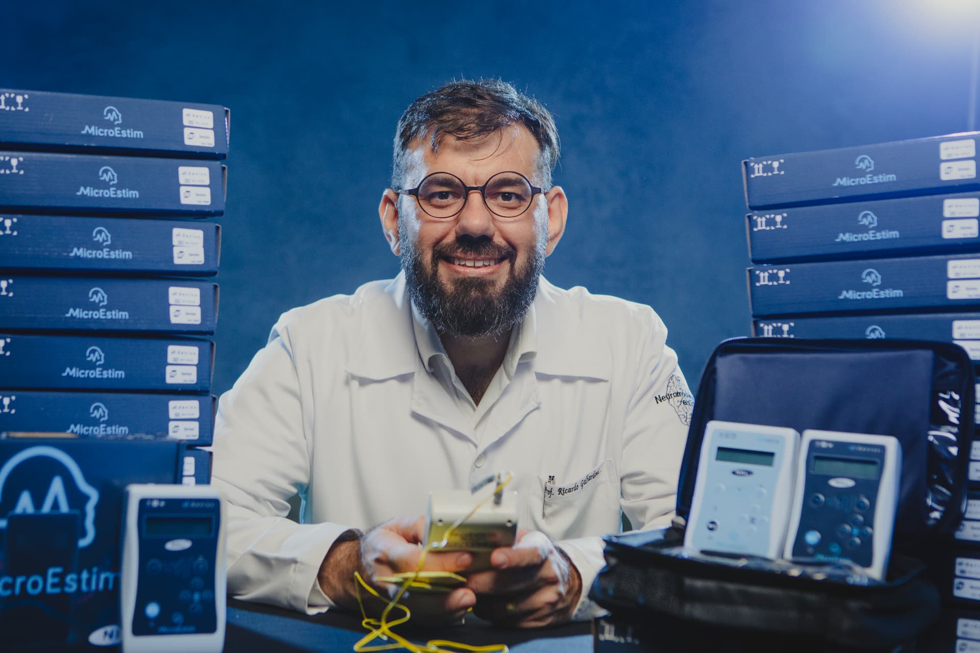 Prof. Dr. Ricardo Galhardoni cercado por equipamentos e caixas de aparelhos de tDCS
